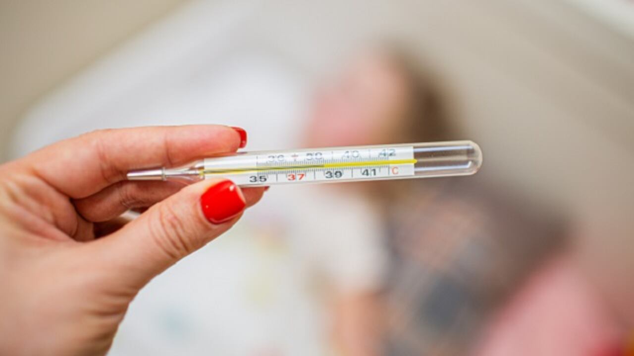 Womans hand holding mercury thermometer on the background of a sick child.