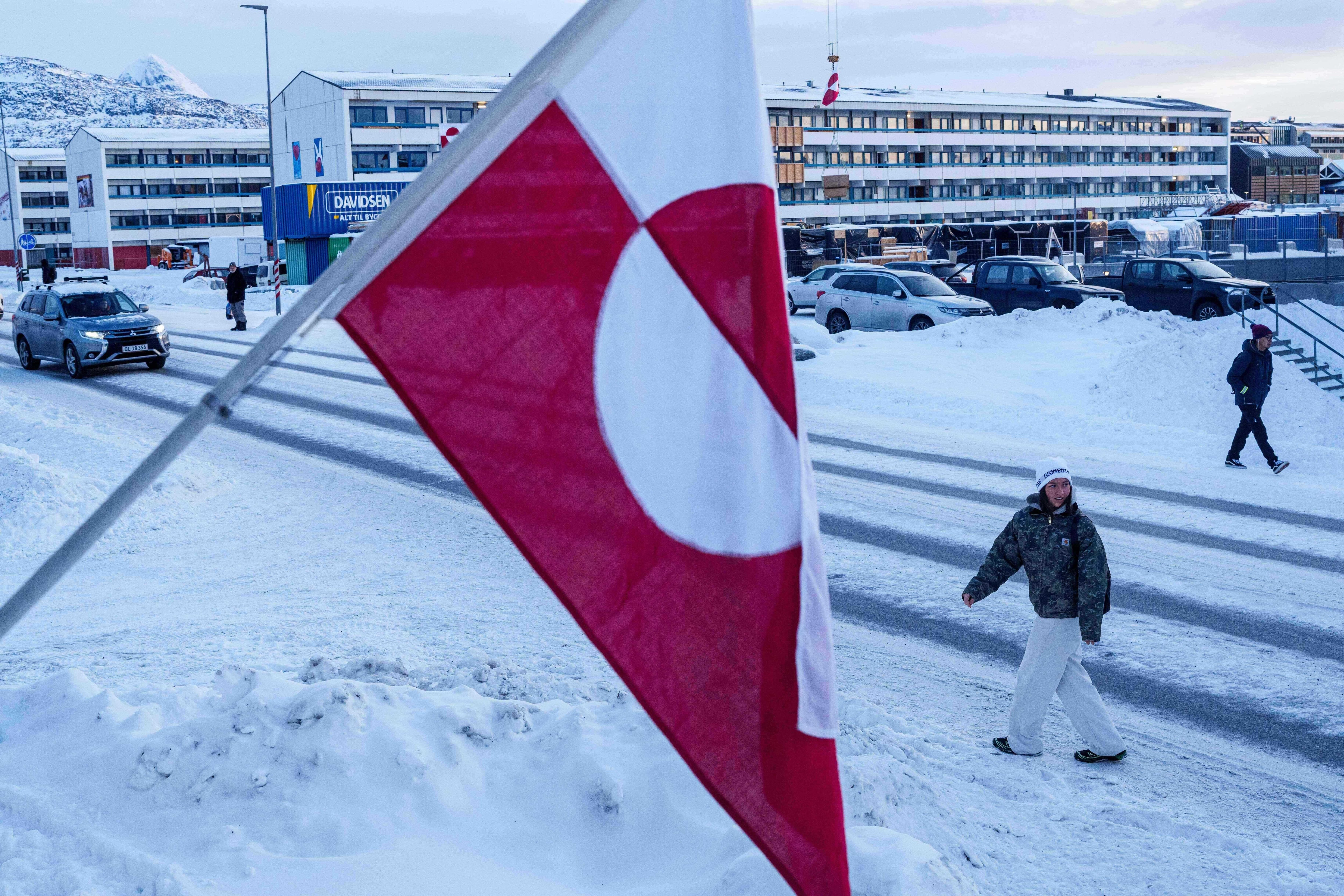Una mujer camina frente a la bandera nacional de Groenlandia en Nuuk, la capital de la isla.