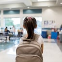 Elementary schoolgirl enters the school cafeteria. She pauses while looking for a friend.