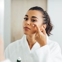 Beautiful woman in bathrobe applying anti-aging cream on her cheek