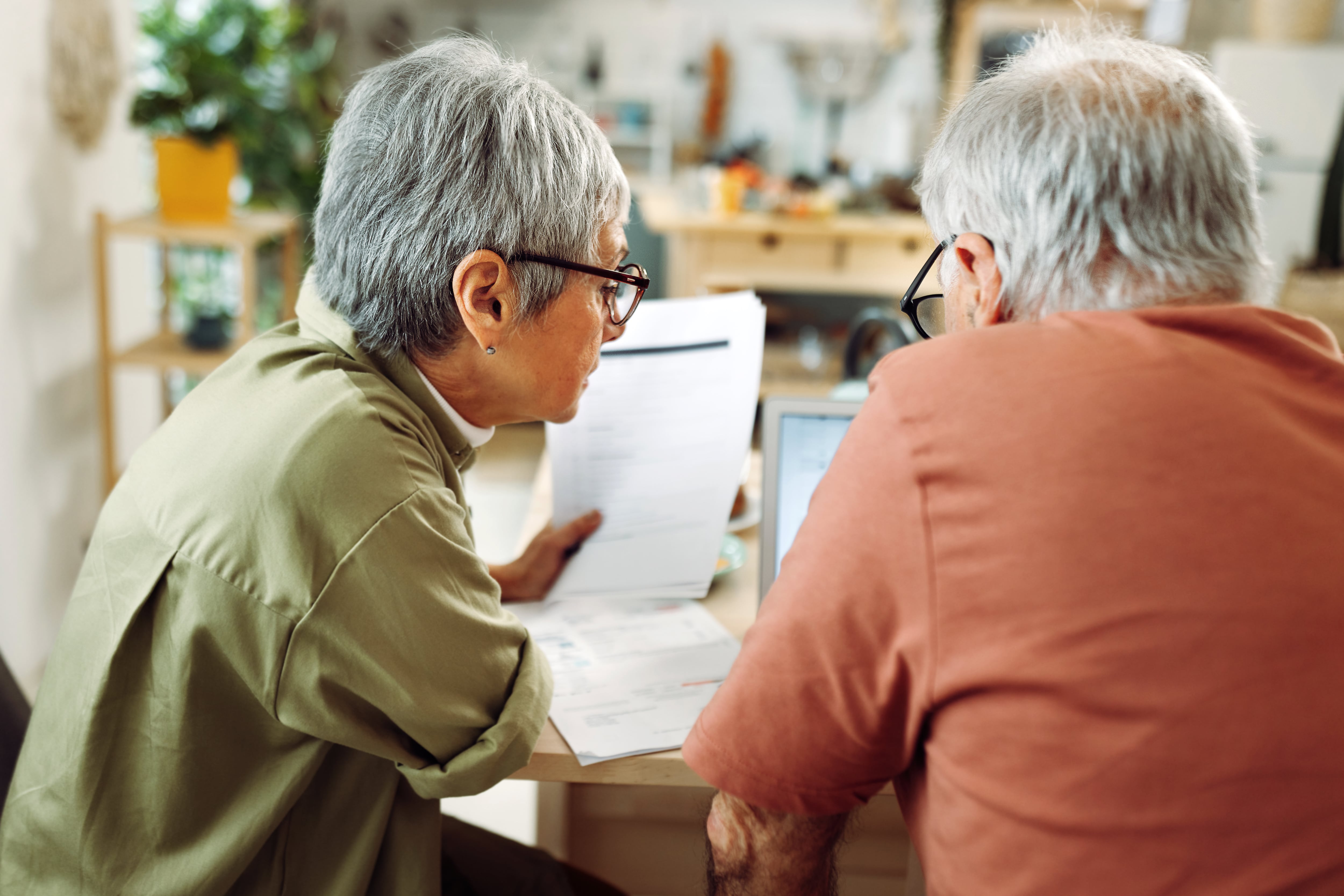 Rear view of casually clothed senior couple going over paperwork at home