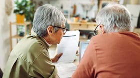 Rear view of casually clothed senior couple going over paperwork at home