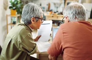 Rear view of casually clothed senior couple going over paperwork at home