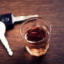 A shot glass full of dark colored alcohol on top of a bar table along with a set of car keys. Drinking and driving series. Also driving under the influence of alcohol.