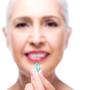 selective focus of attractive smiling senior woman with pill, isolated on white