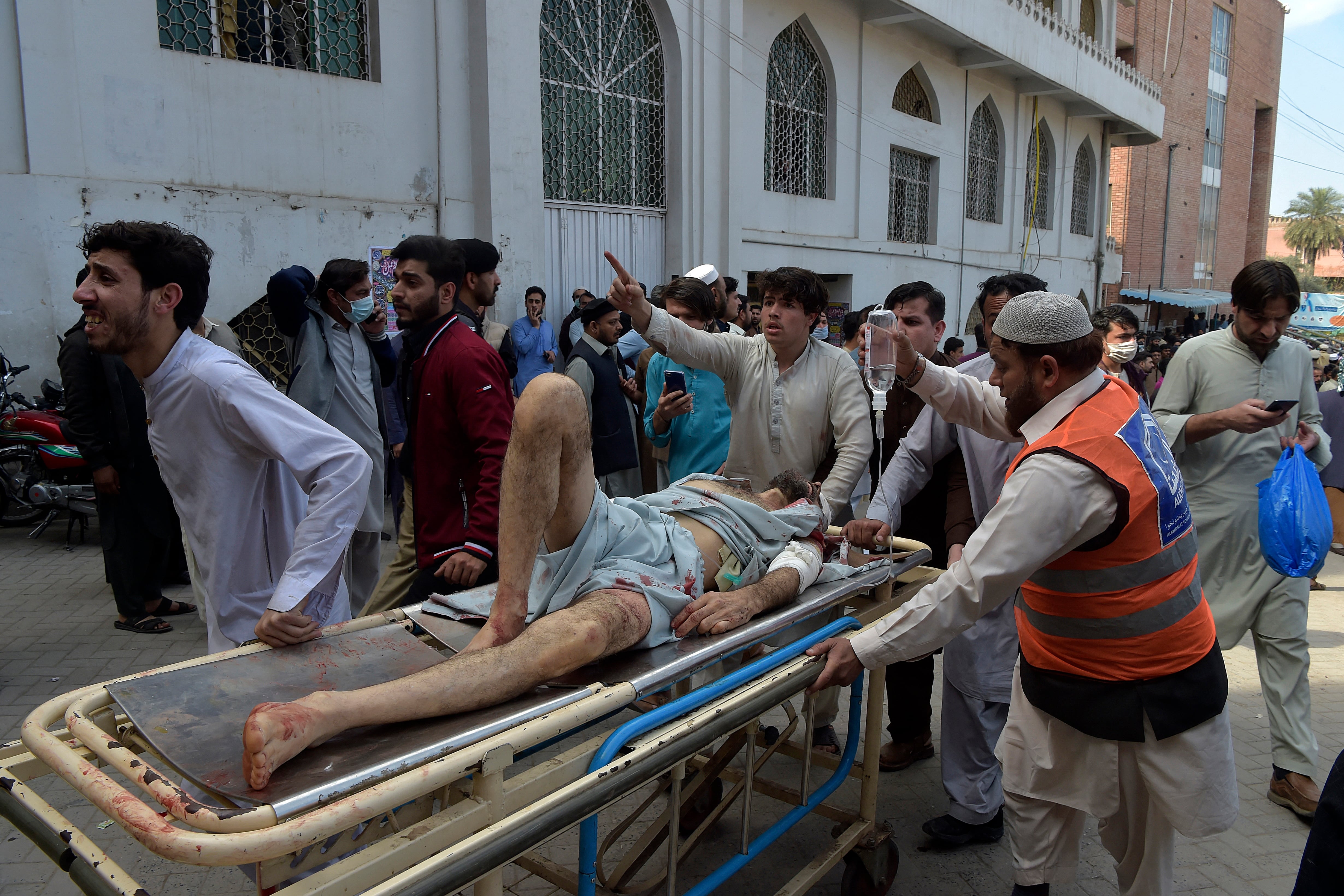 La gente ayuda a sacar a una víctima fuera de un hospital tras la explosión de una bomba en una mezquita en Peshawar el 4 de marzo de 2022. - Al menos 30 personas murieron y 56 resultaron heridas en una gran explosión en una mezquita en la ciudad de Peshawar, en el noroeste de Pakistán. dijo un funcionario del hospital el 4 de marzo. (Foto de Abdul MAJEED / AFP)