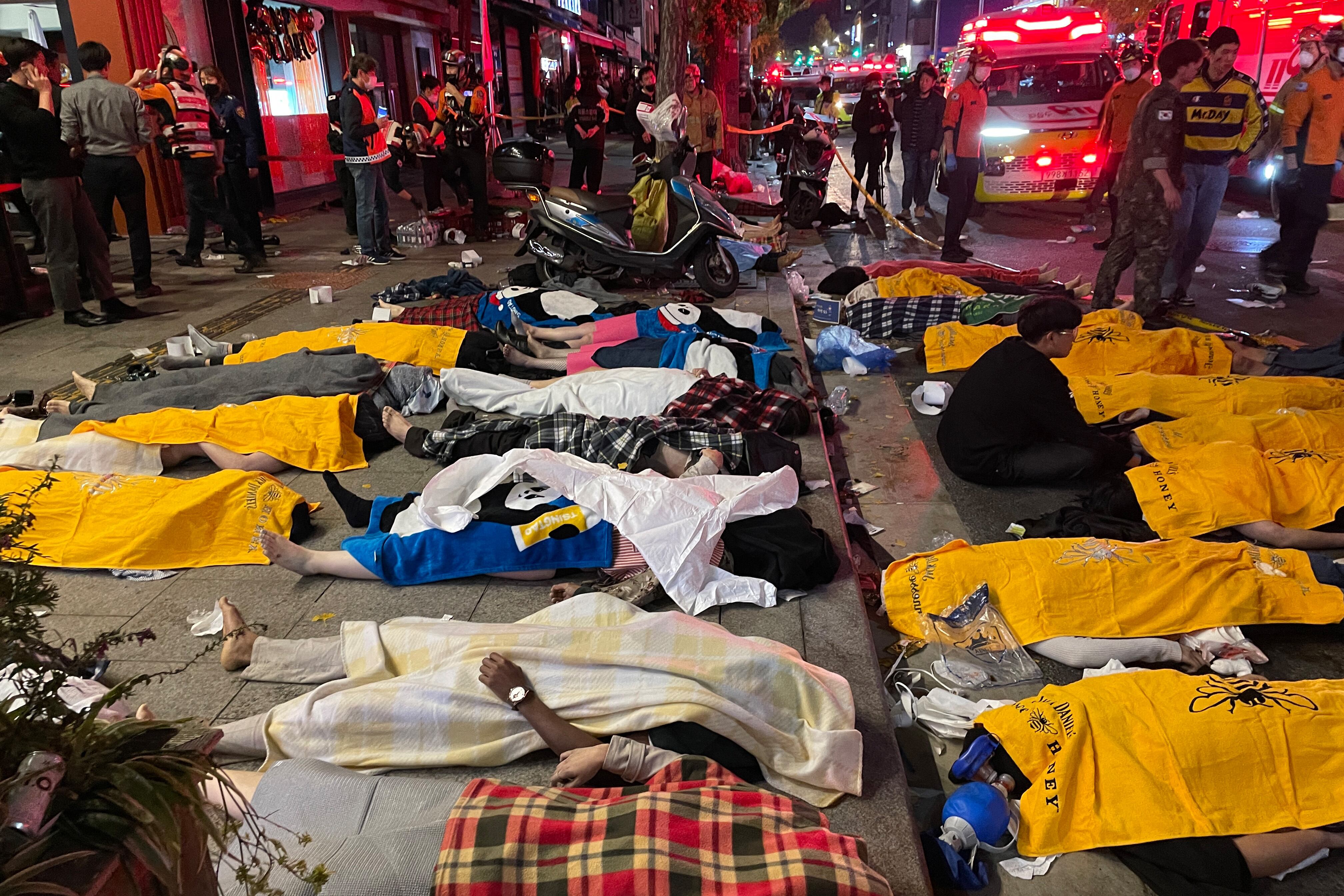 Un hombre se sienta en medio de los cuerpos de las víctimas, que se cree que sufrieron un paro cardíaco, en el popular distrito de vida nocturna de Itaewon en Seúl el 30 de octubre de 2022. - Decenas de personas sufrieron un paro cardíaco en la capital de Corea del Sur. Seúl, después de que miles de personas se aglomeraran en las estrechas calles del barrio Itaewon de la ciudad para celebrar Halloween, dijeron funcionarios locales. (Foto de Yelim LEE / AFP)
