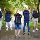 Rear-view of five children jumping in the air wearing backpacks
