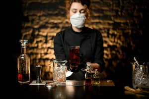 Foto de referencia de licor en medio de una mujer con tapabocas puesto