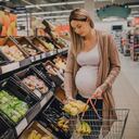 A young pregnant woman is grocery shopping in a supermarket store.