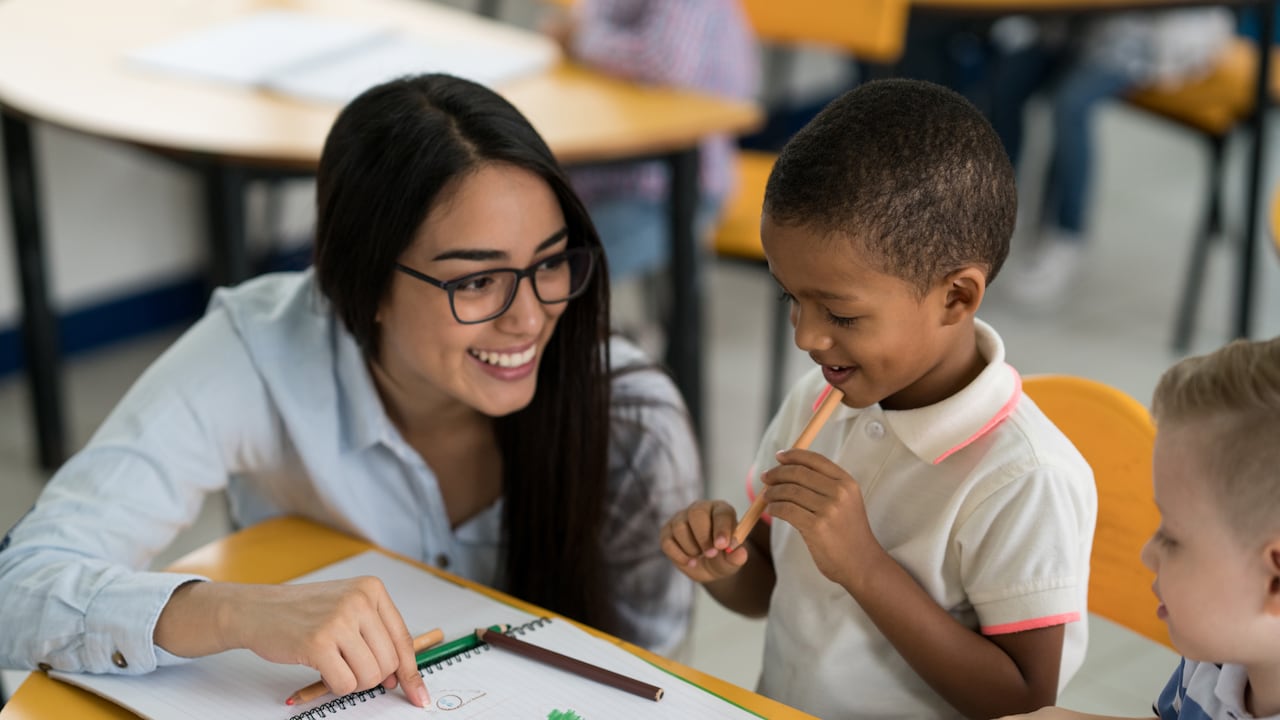 Retrato de un profesor latinoamericano feliz que mira los dibujos de dos niños en la escuela - conceptos de la educación