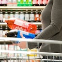 Mujer comparando ingredientes en botella de refresco, botella de gaseosa