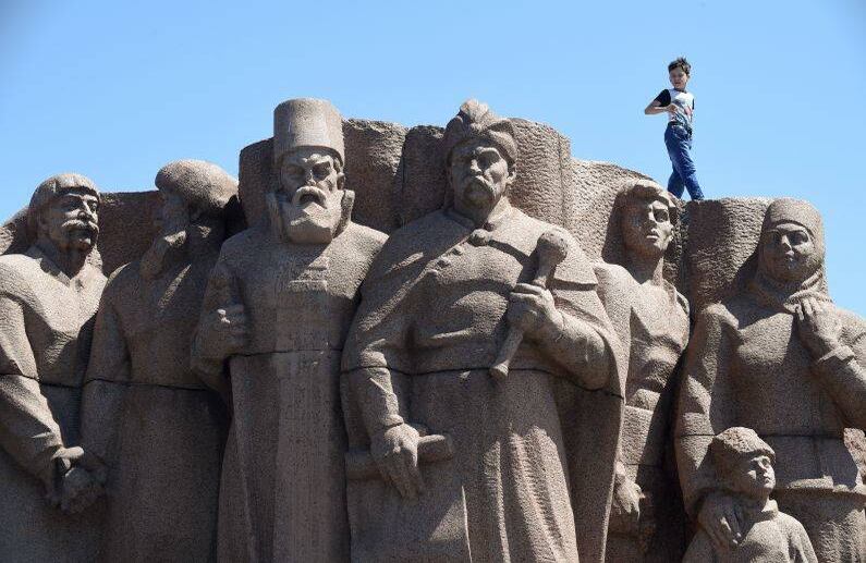 Un niño camina en la cima de un monumento de la era de la Unión Soviética en Kiev, Ucrania, el 1 de julio de 2019. (Foto de Sergei SUPINSKY / AFP)