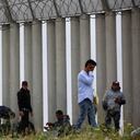 Migrantes llegan a la frontera para pedir asilo a autoridades estadounidenses entre los muros fronterizos.