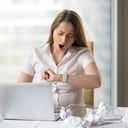 Joven empresaria bostezando mientras trabaja en una laptop en la oficina. Empresaria soñolienta mirando el reloj de pulsera. El oficinista cansado siente falta de sueño debido al trabajo duro y prolongado con documentos