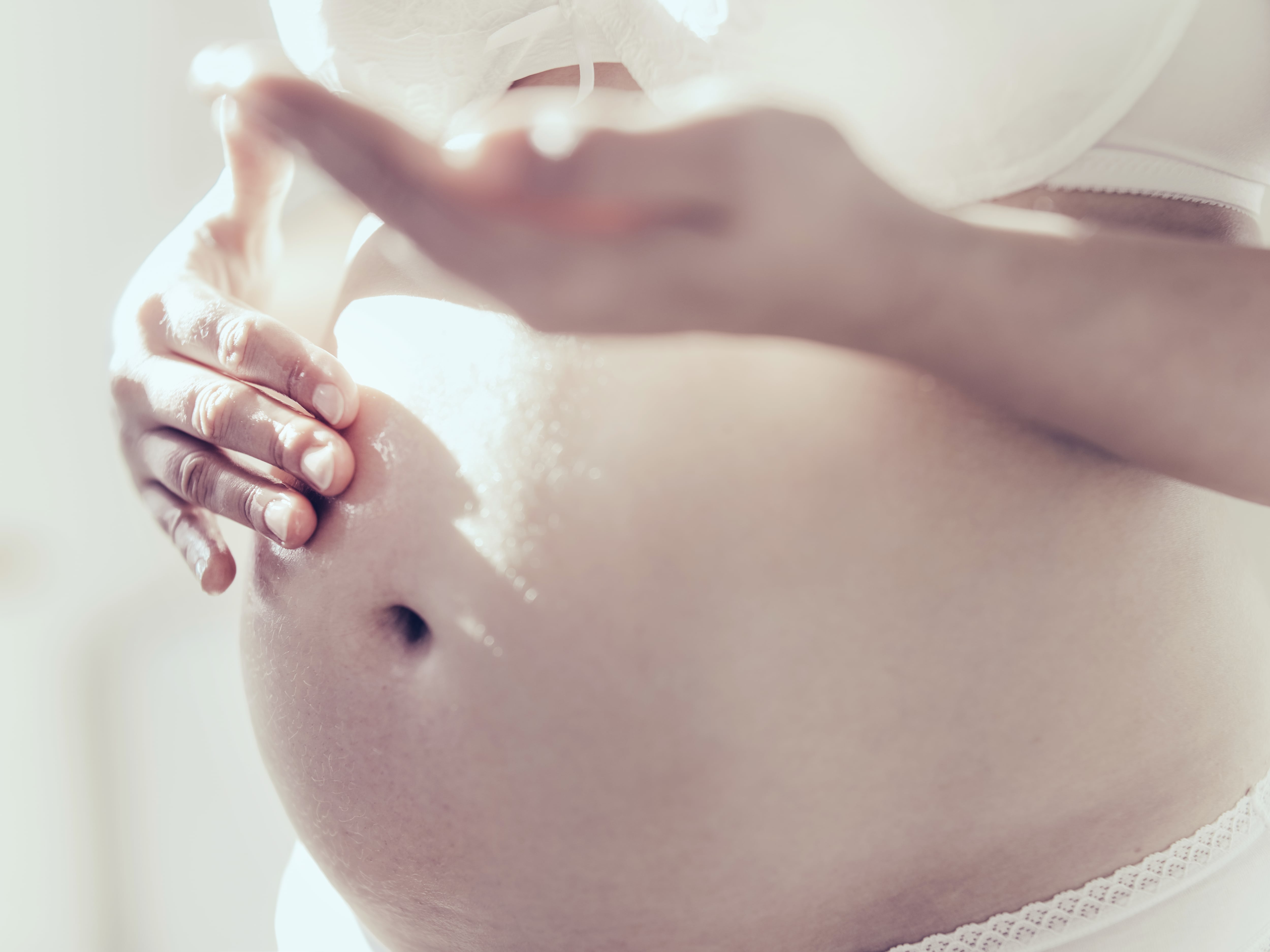 Pregnant woman rubbing oil on her belly, close up.