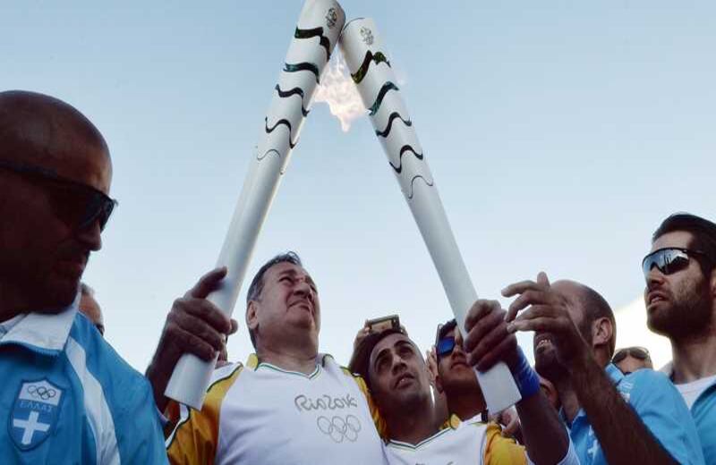 Un refugiado sirio lleva la Llama Olímpica, entregada por el presidente del comité Spyros Kapralos. El refugiado, que recibió asilo en Grecia, era un nadador atlético hasta que perdió una pierna en un bombardeo.