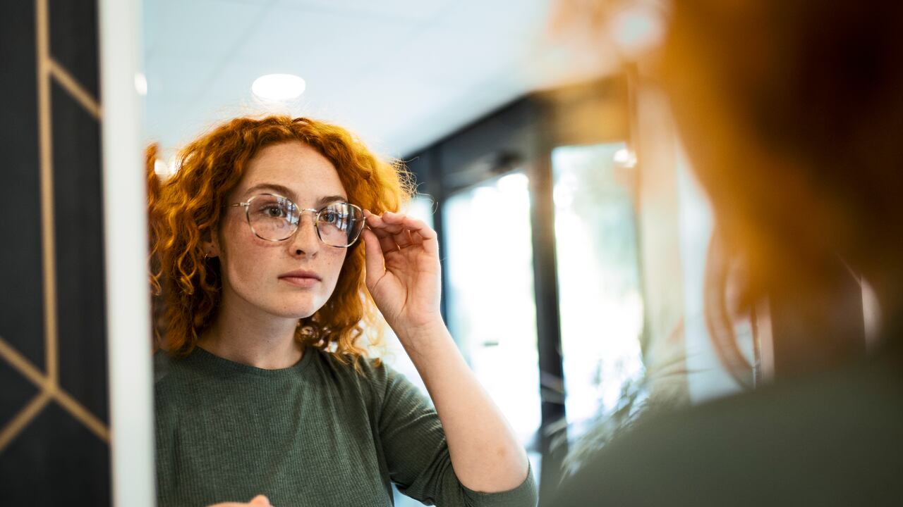 young woman trying on glasses on mirror in optician