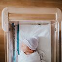 Un bebé recién nacido en el hospital descansa en una cuna de bassinet de hospital, envuelta en un swaddle y con un sombrero de gorro.