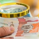 Colombian money held in the hand and viewed through a lupe, business and economic concept