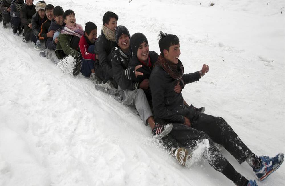 En una hilera y sin dejar de sonreír, niños juegan en la nieve en las afueras de Kabul, Afganistán, viernes, 24 de enero de 2020. Foto: Rahmat Gul/AP.