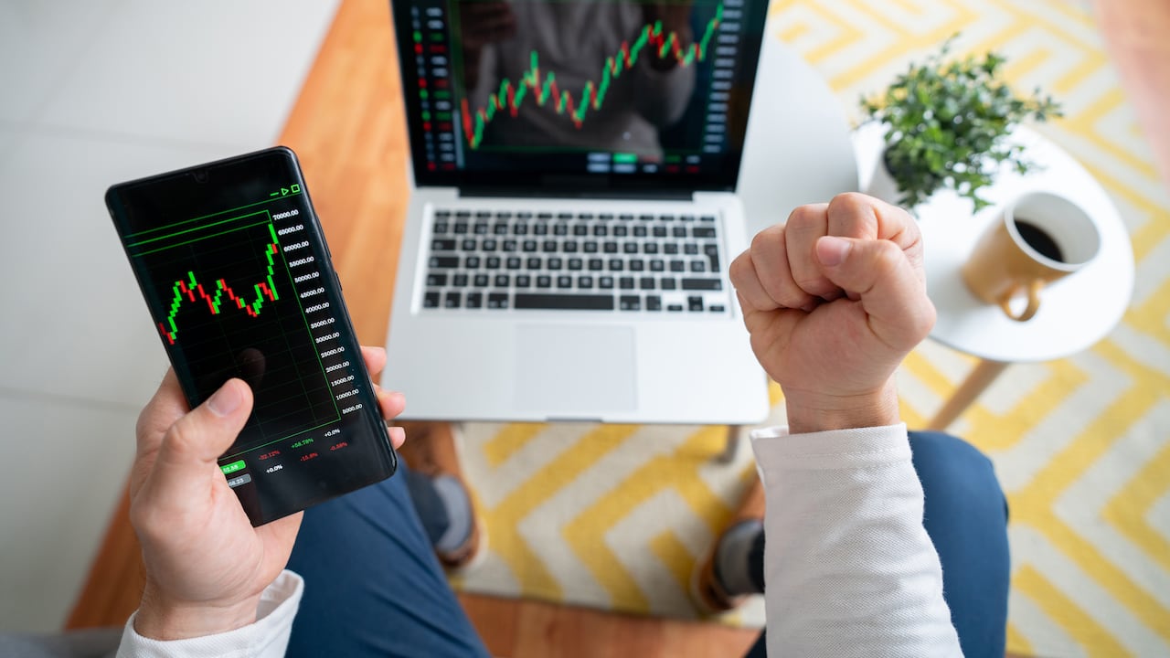 Close-up on an excited man at home looking at his investments in the stock market on his laptop and his cell phone