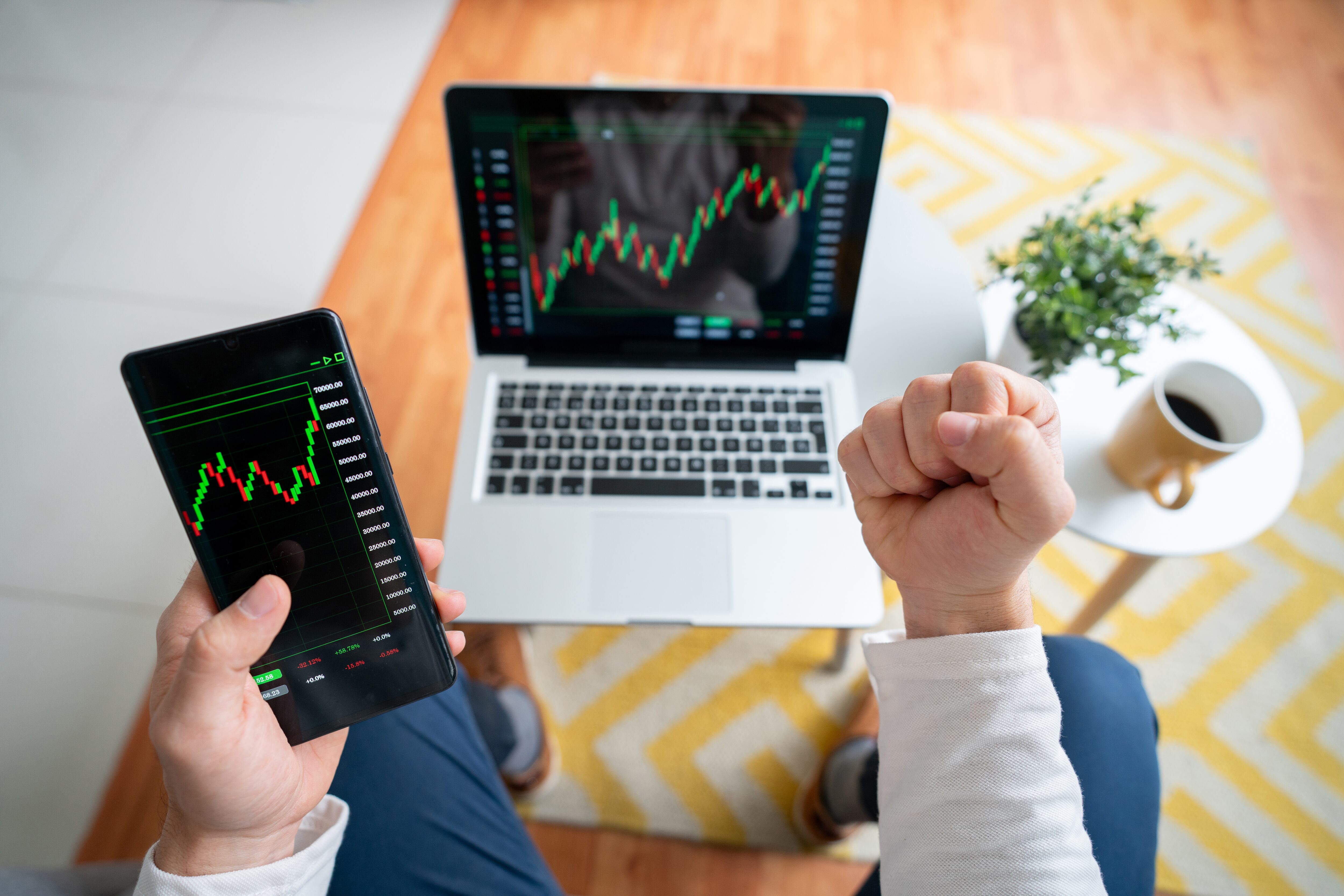 Close-up on an excited man at home looking at his investments in the stock market on his laptop and his cell phone