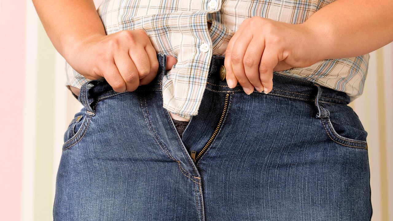 Adolescente obesa apretando un par de jeans demasiado apretados.