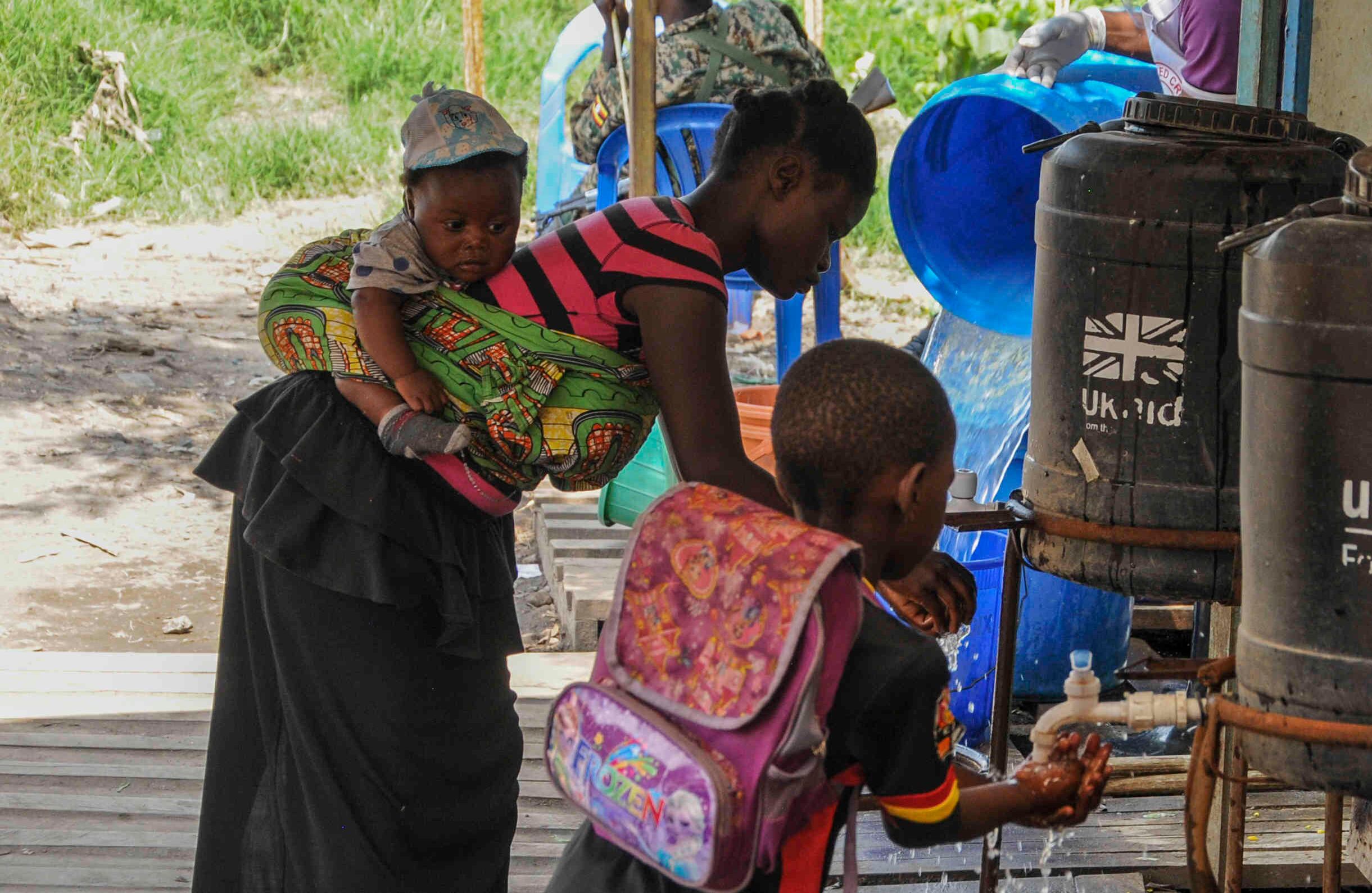 Las personas que vienen del Congo se lavan las manos con agua clorada para prevenir la propagación de la infección, en el cruce de la frontera de Mpondwe con el Congo, en el oeste de Uganda, el viernes 14 de junio de 2019.  (AP Photo/Ronald Kabuubi)
