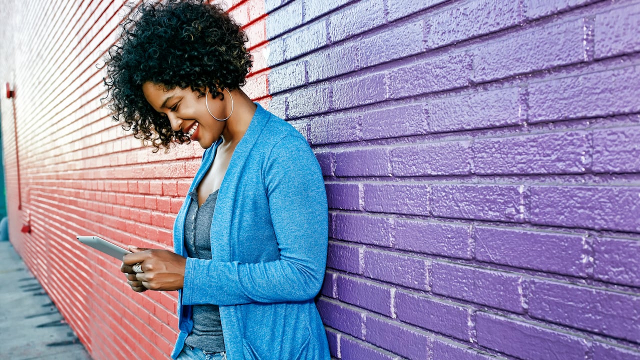 Mixed race woman with cell phone standing by colorful wall