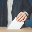 Votante masculino irreconocible sostiene en su mano una boleta sobre la urna