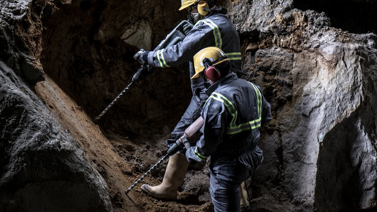 Dos trabajadores con casco y traje de protección mediante taladradoras en un entorno subterráneo