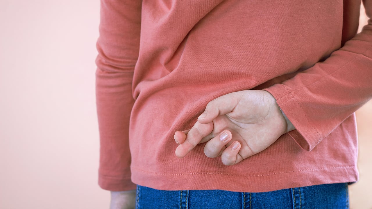 Niña cruzando los dedos detrás de la espalda sobre un fondo claro con espacio para copiar. Mentira y engaño, concepto mentiroso. Día de los Inocentes