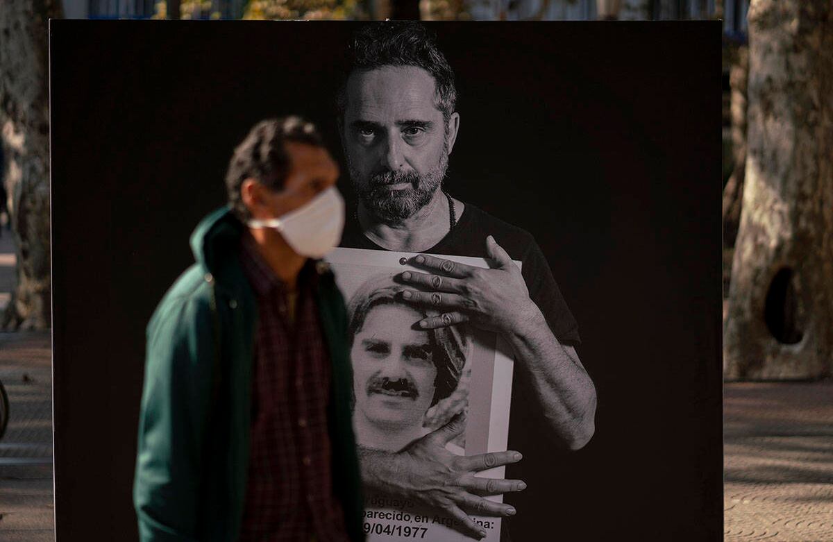 Un hombre con una máscara facial pasa una foto grande del cantante y compositor uruguayo Jorge Drexler, quien tiene una foto más pequeña de Andrés Bellizzi, desaparecido durante la dictadura militar (1973-1985), en el centro de Montevideo, Uruguay el miércoles 20 de mayo de 2020, día en que dos legisladores fueron asesinados en 1976. El miércoles se cumple el 25 aniversario de una marcha anual que recuerda a los desaparecidos y asesinados durante la dictadura, pero la marcha de este año no se llevará a cabo debido a las medidas para contener la propagación del nuevo coronavirus. (Foto AP / Matilde Campodonico)