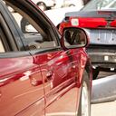 Two-car accident. Focus on the interior and mirror of red car. Two ladies inside are reflected in mirror. Wrecked vehicles. Crushed bumper, rear of car.