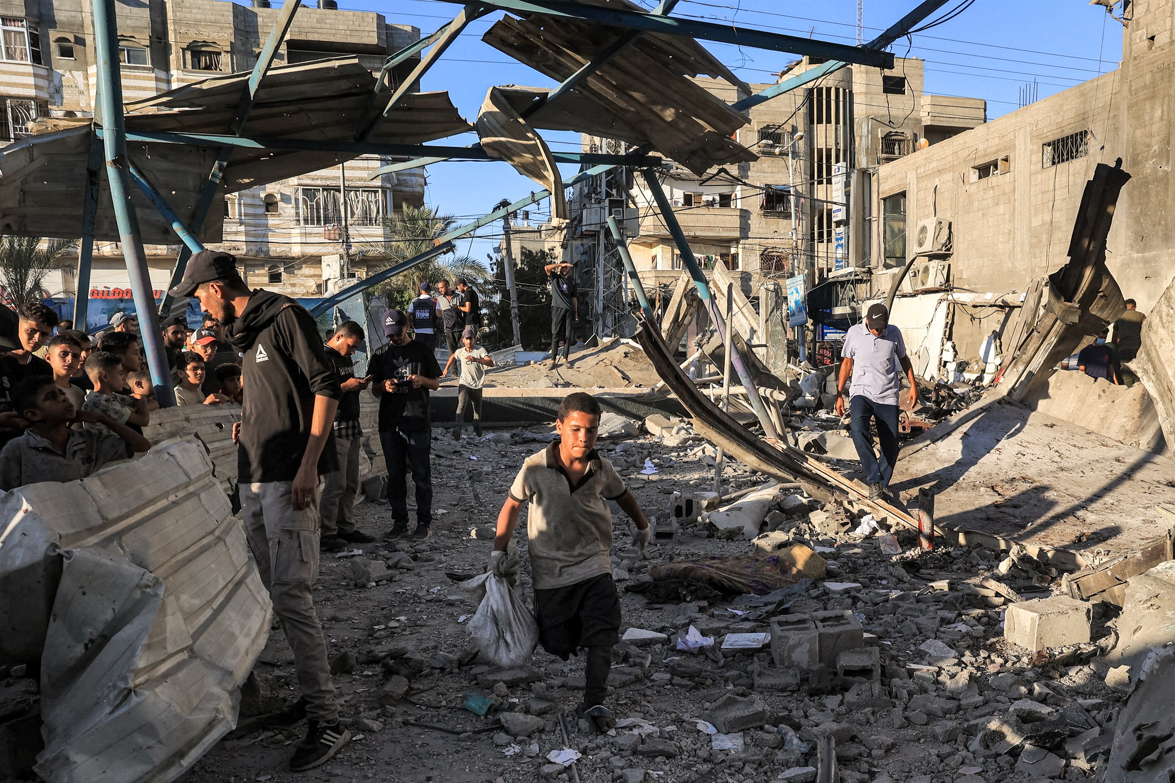 A boy runs with a sack as people search the rubble of a collapsed building in the aftermath of Israeli bombardment at the Jaouni school run by the UN Relief and Works Agency for Palestine Refugees (UNRWA) in Nuseirat in the central Gaza Strip on July 6, 2024 amid the ongoing conflict in the Palestinian territory between Israel and Hamas. (Photo by Eyad BABA / AFP)