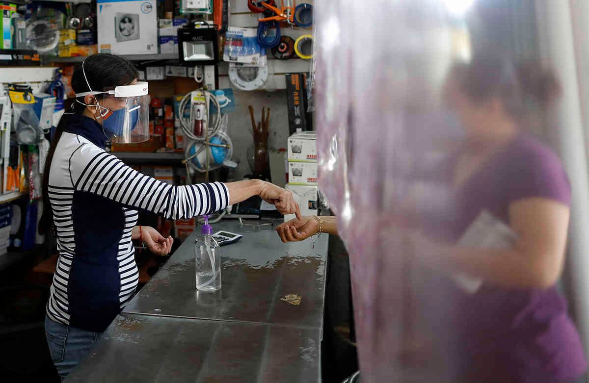 Carmen Castellanos, de 54 años, atiende en la ferretería y la tienda de suministros eléctricos El Foquito a una cliente que asoma su mano a través de una lámina protectora de plástico que cuelga sobre el mostrador, en el distrito Benito Juárez de Ciudad de México, el 15 de abril. En México ya hay más de 8.000 casos confirmados. Foto: Rebecca Blackwell/ AP