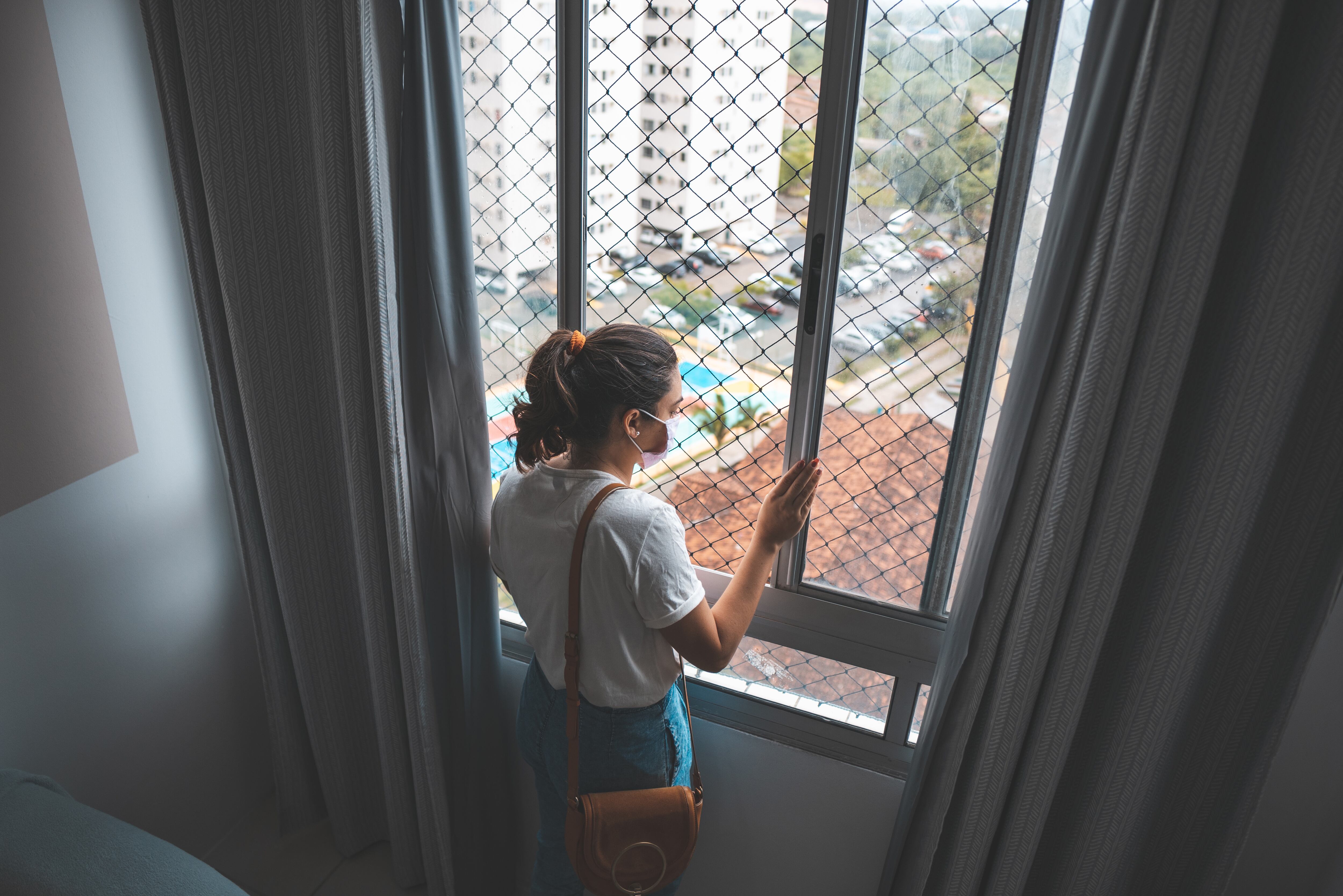 Vista superior de la mujer mirando por la ventana con una mascarilla