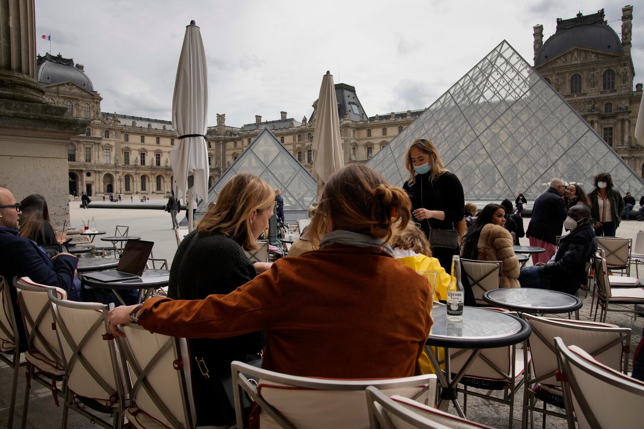 La gente toma un café al aire libre en un bar frente al museo del Louvre en París, el jueves 20 de mayo de 2021. AP Photo/Christophe Ena