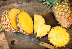 one whole and one sliced pineapples on wooden bEsta deliciosa fruta tropical tiene un sabor único y también grandes beneficios para la salud. ackground
