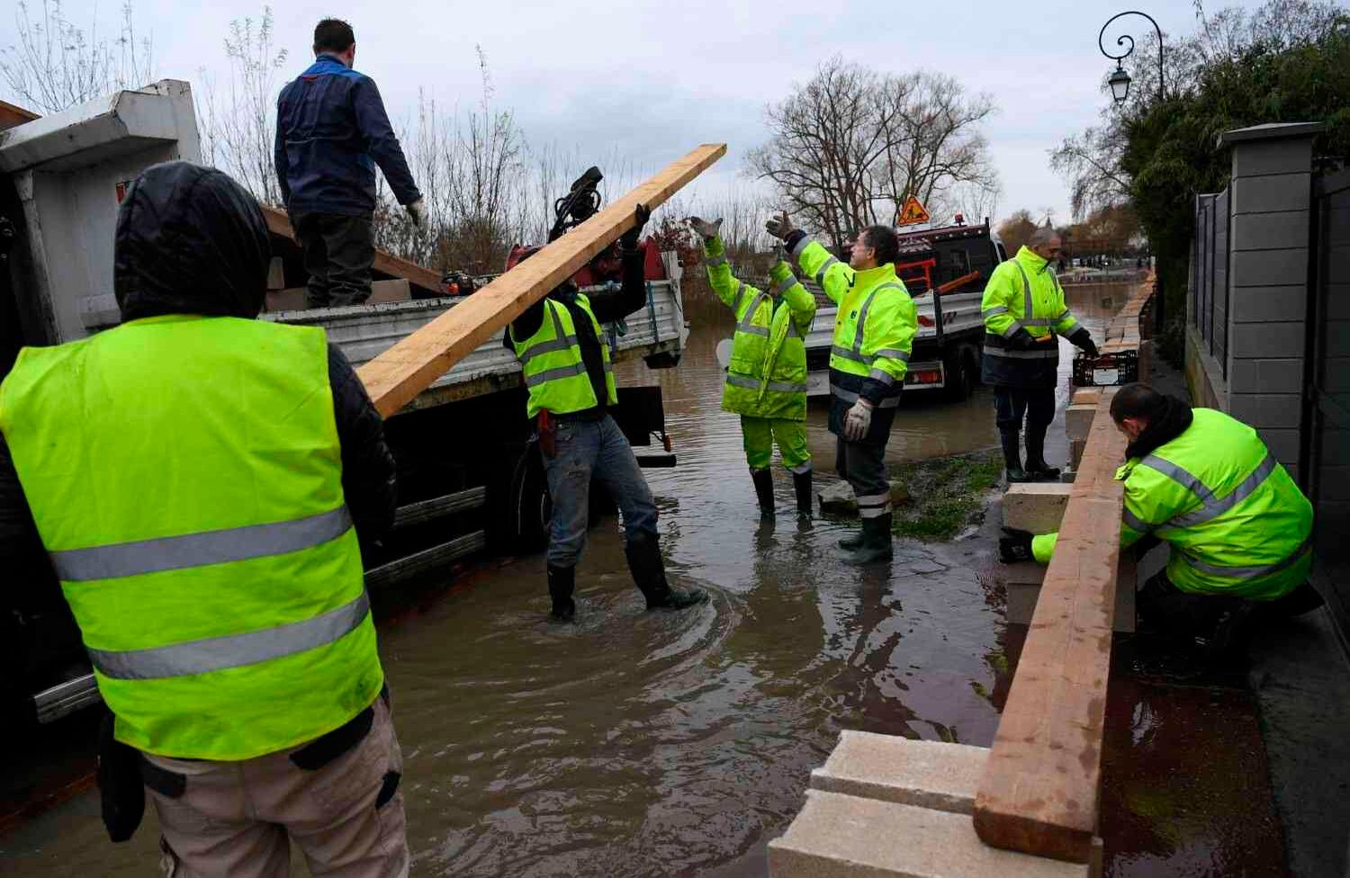 Los trabajadores llevan bloques de brisa y tablones para construir una pasarela de madera elevada para cruzar una sección inundada de una calle en Conflans-Sainte-Honorine, en las afueras de París, el 25 de enero de 2018, mientras el Sena continuaba elevándose.  / AFP PHOTO / Christophe Archambault.