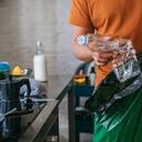 Apuesto joven sosteniendo una bolsa de basura verde y una botella de plástico