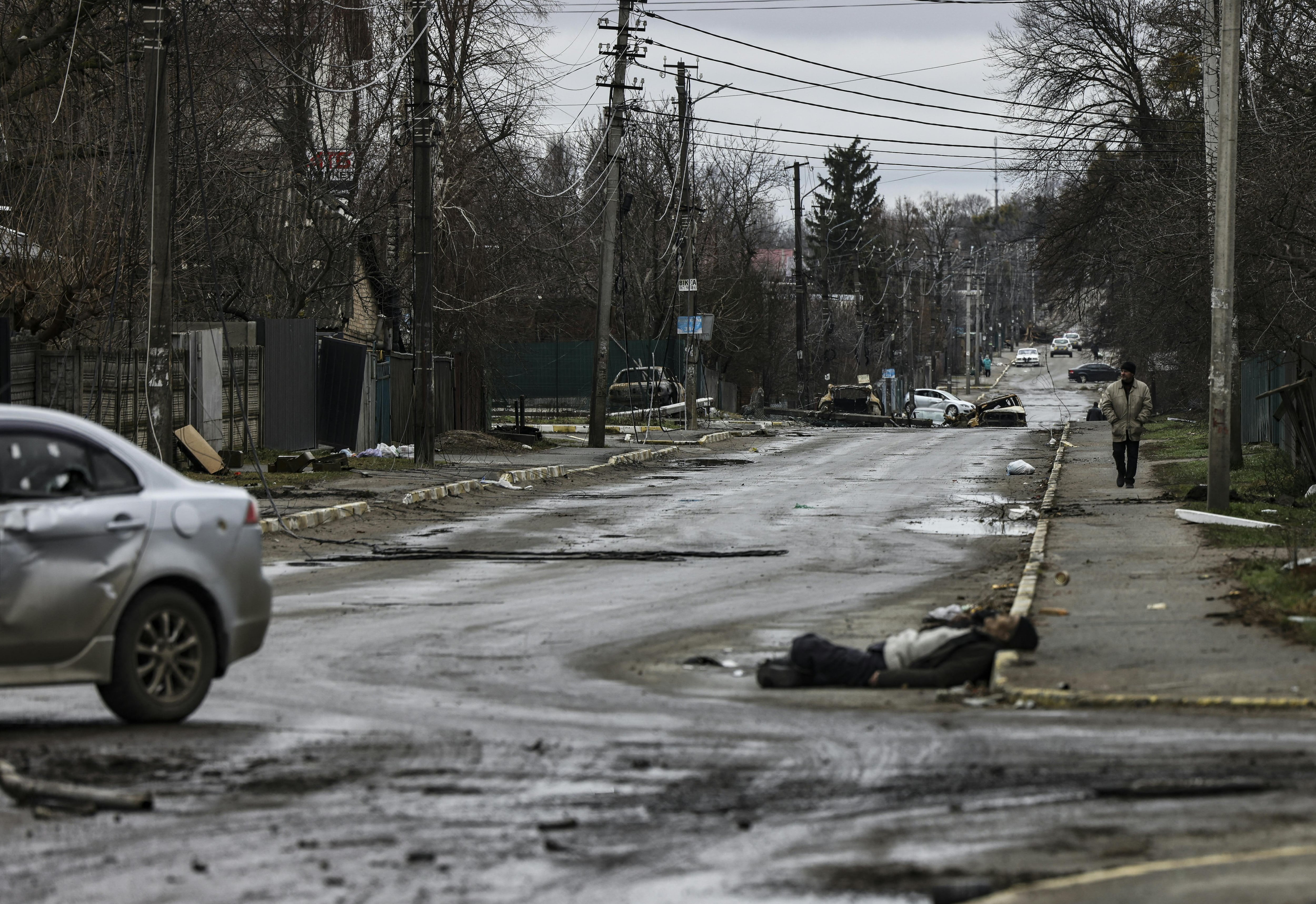 EDITORS NOTE: Graphic content / A man walks on a street with several dead bodies on the ground a street in Bucha, northwest of Kyiv, as Ukraine says Russian forces are making a "rapid retreat" from northern areas around Kyiv and the city of Chernigiv, on April 2, 2022. - The bodies of at least 20 men in civilian clothes were found lying in a single street Saturday after Ukrainian forces retook the town of Bucha near Kyiv from Russian troops, AFP journalists said. Russian forces withdrew from several towns near Kyiv in recent days after Moscow's bid to encircle the capital failed, with Ukraine declaring that Bucha had been "liberated". (Photo by RONALDO SCHEMIDT / AFP)