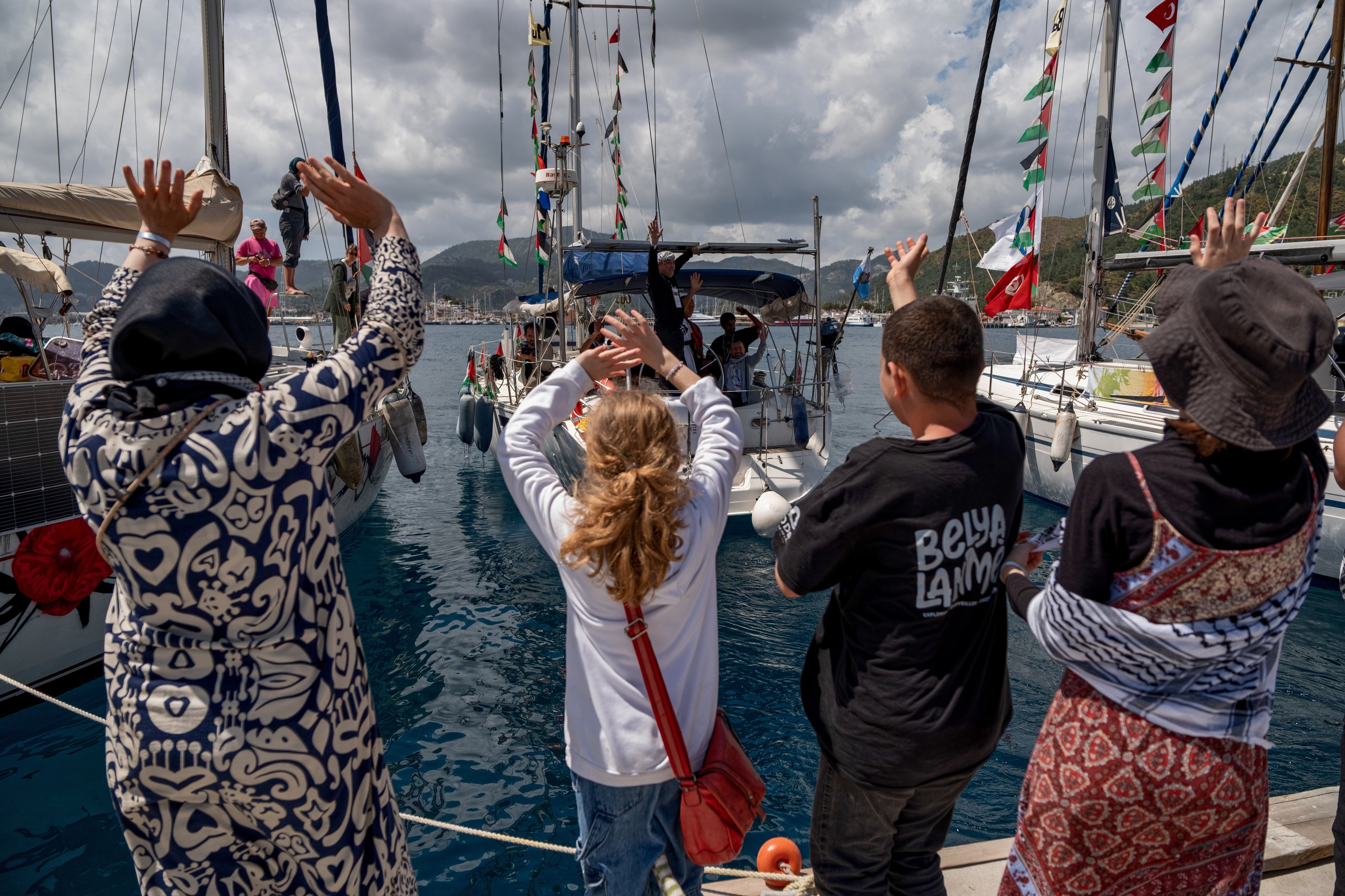 Varias personas saludan a las embarcaciones de la Flotilla Global Sumud, que transportan activistas y ayuda humanitaria, mientras parten hacia Gaza desde el puerto de Marmaris, Turquía.