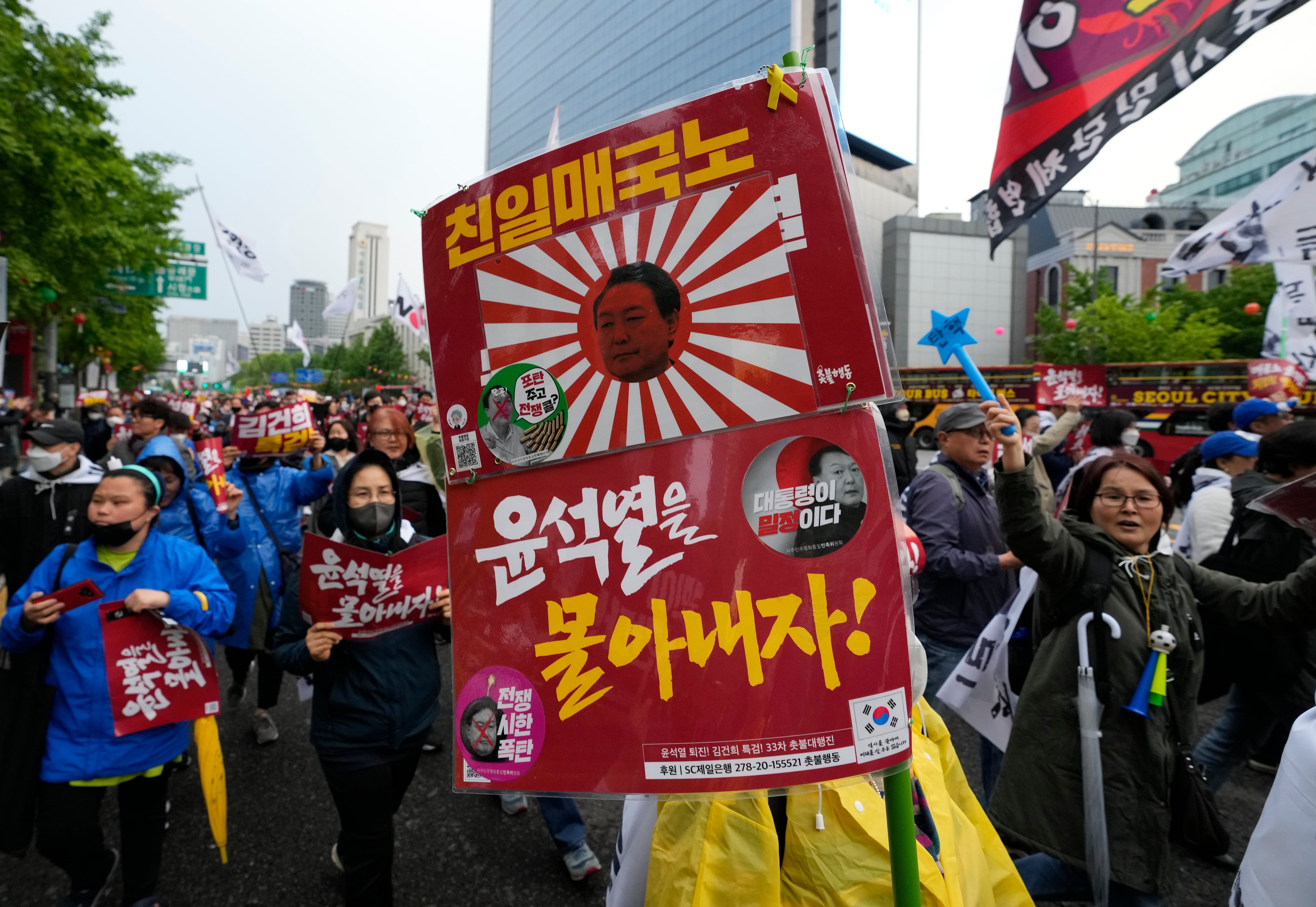 Numerosos manifestantes cargan un cartel con la imagen del presidente surcoreano Yoon Suk Yeool proyectada en una antigua bandera imperial del ejército japonés, durante una protesta contra las políticas del gobierno japonés, efectuada en Seúl, Corea del Sur, el sábado 6 de mayo de 2023. El cartel dice "Traidor projaponés".