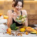 Mujer de deportes comiendo ensalada, de pie con una gran cantidad de alimentos frescos y saludables en la cocina. Concepto de adelgazamiento, deporte y alimentación saludable.