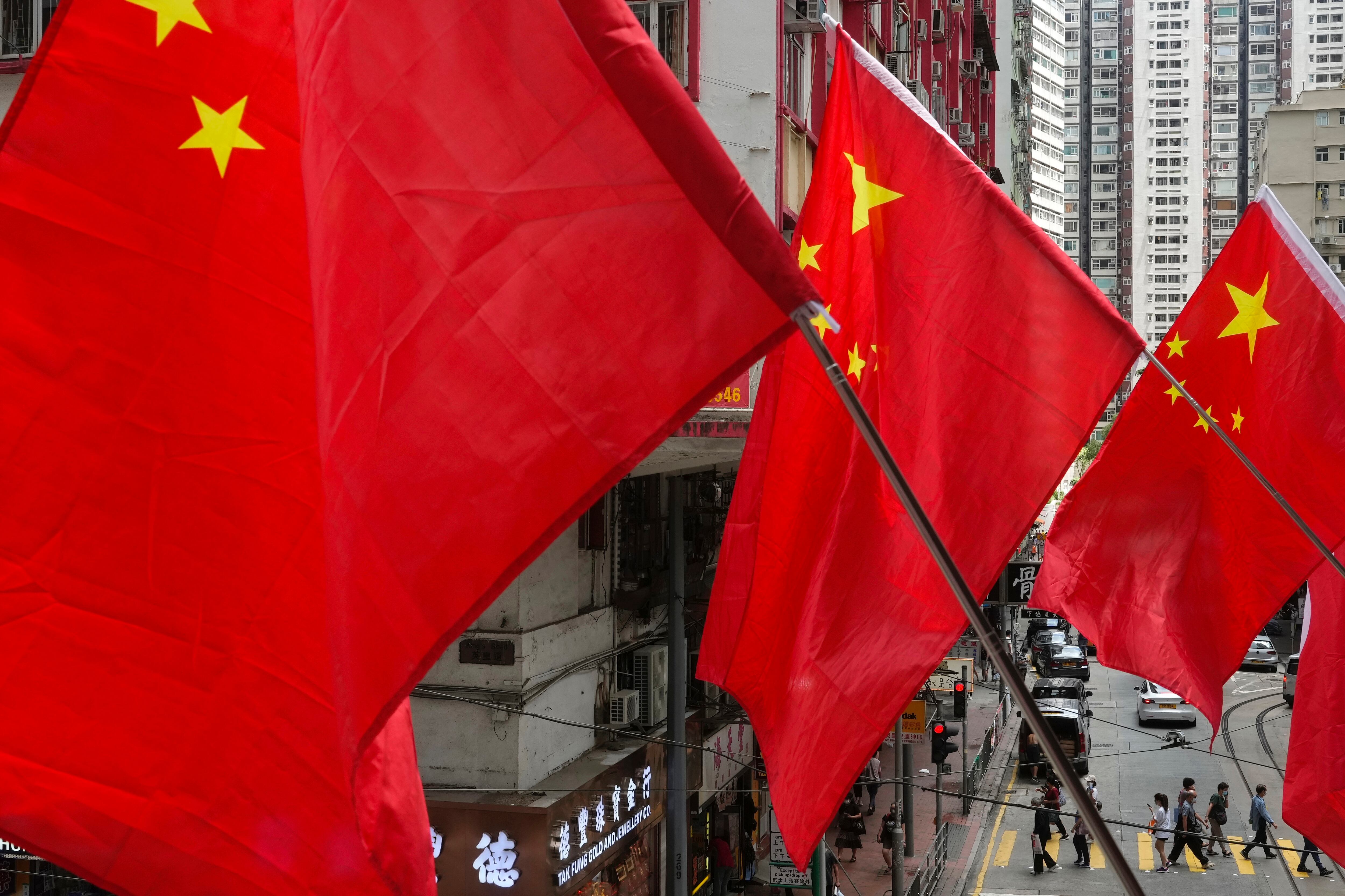 La gente camina bajo las banderas nacionales chinas colocadas en una pasarela para conmemorar el 24º aniversario de la entrega de Hong Kong a China en una escuela de Hong Kong el jueves 1 de julio de 2021. Foto: AP Photo/Vincent Yu