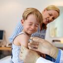 Niño frunciendo el ceño de dolor mientras recibe una vacuna en su brazo. Pediatra vacunando a un niño sentado con su madre en la clínica. covid