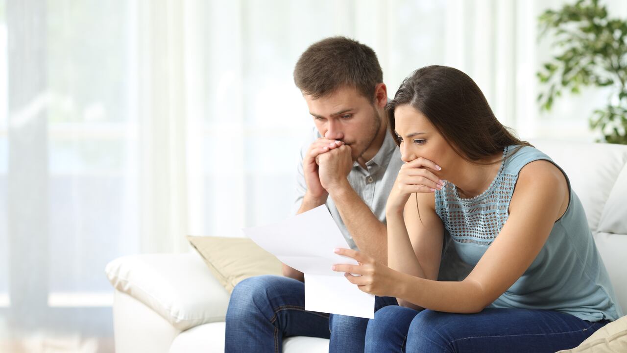 Worried couple reading an important notification in a letter sitting on a couch in the living room at home