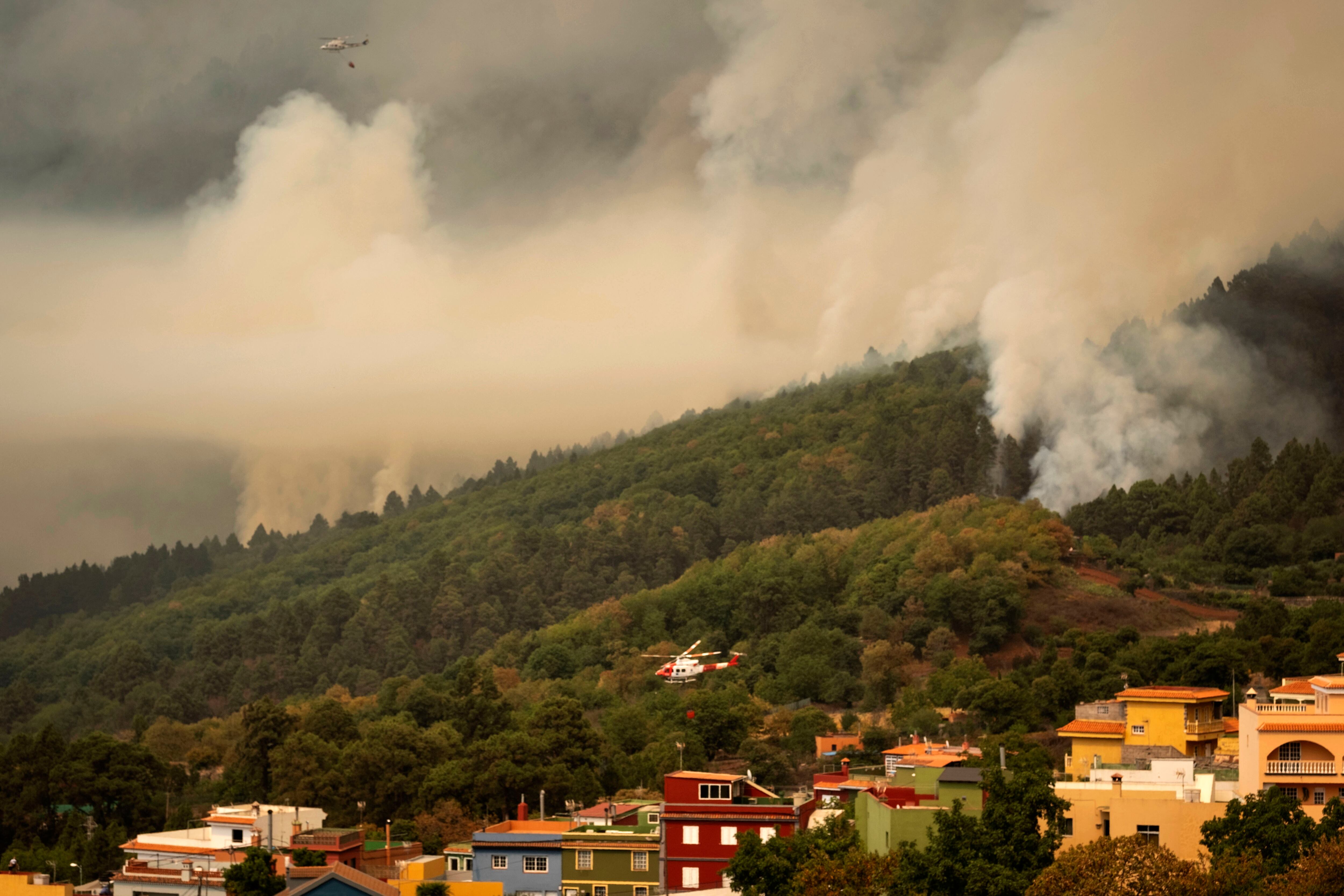 Un helicóptero arroja agua sobre las llamas mientras el fuego avanza a través del bosque hacia la ciudad de El Rosario en Tenerife, España, el viernes 18 de agosto de 2023.